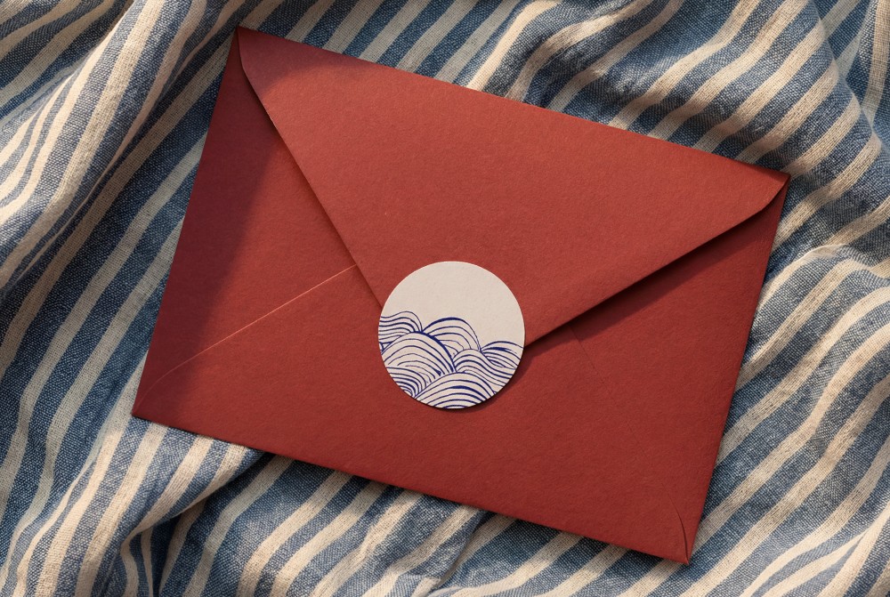 Vintage rood envelop met sluitzegel en handgetekende golven van de zee bij geboortekaartje Joa