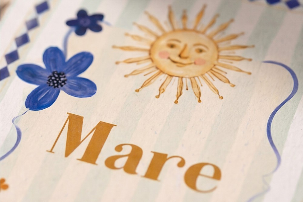 Detail van geboortekaartje Mare met ruitjeskader, zachte streepjes en handgeschilderde illustraties.